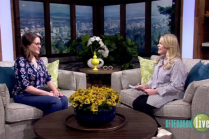 Two women are sitting on a couch, talking animatedly. Behind them is a wooden wall with shelves holding various decorative items. A green pillow with a white design is on the couch beside them. The logo "afternoon live" is displayed in the bottom right corner. The women appear to be in a television studio setting, engaging in a lively conversation.